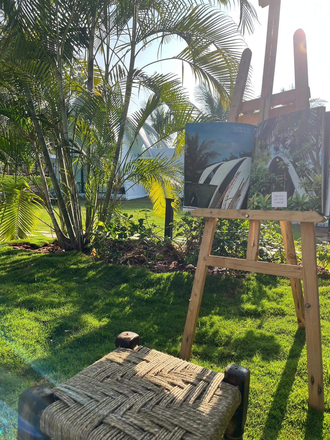An easel and a woven stool set out on the garden lawn