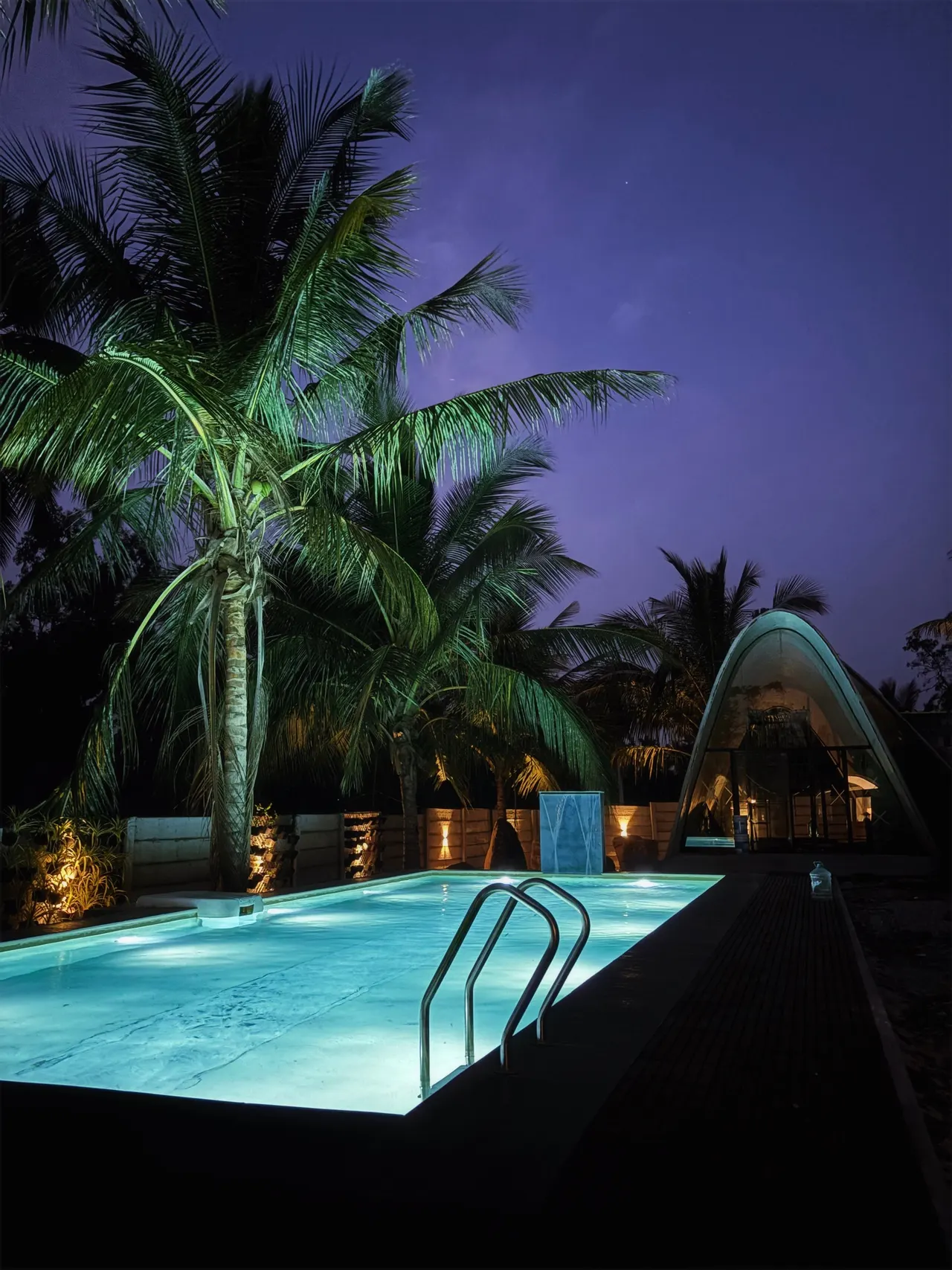 The turquoise pool, lit at night beneath palms beside a shell