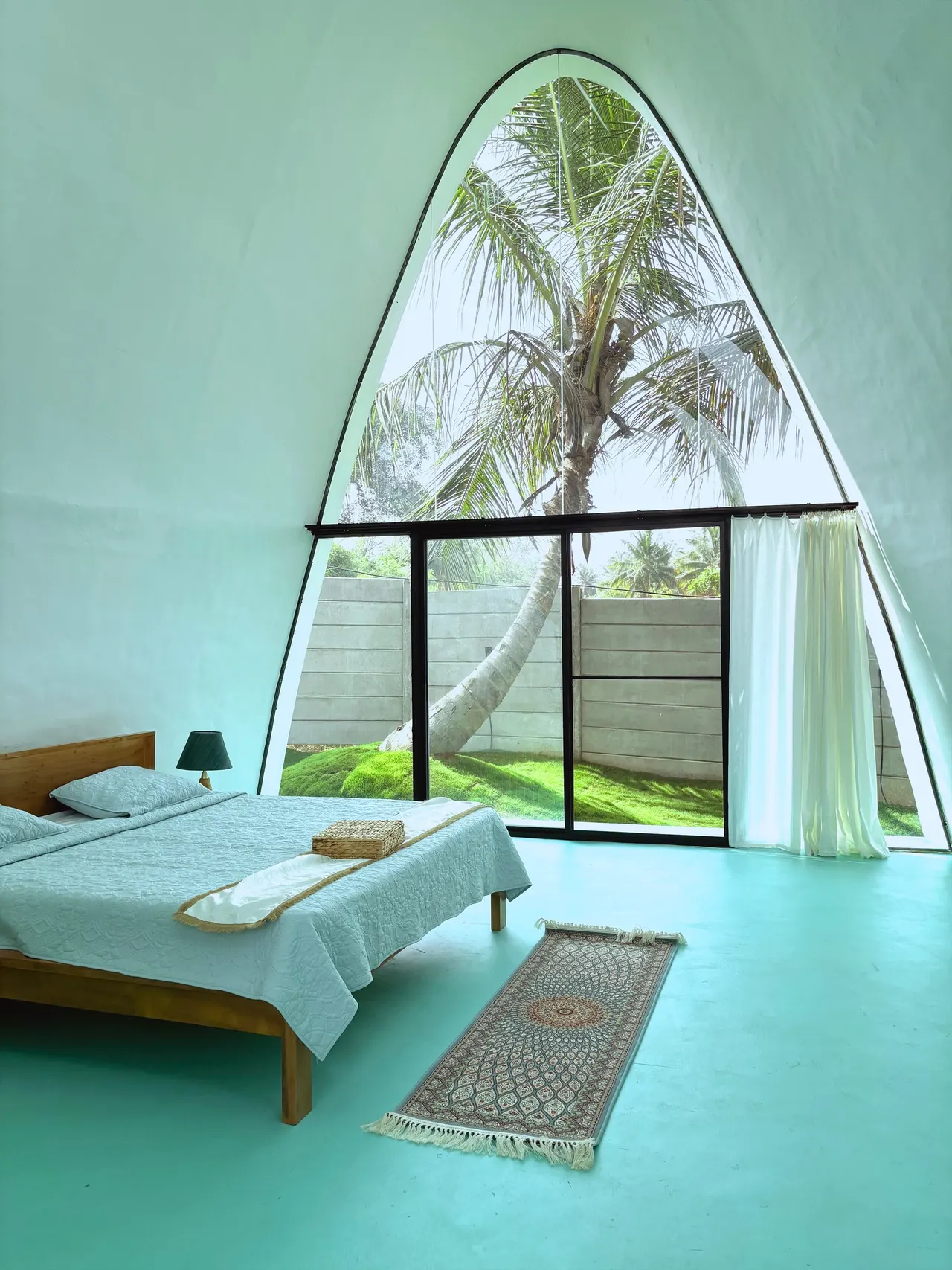 Villa bedroom with a pointed-arch window framing a coconut palm