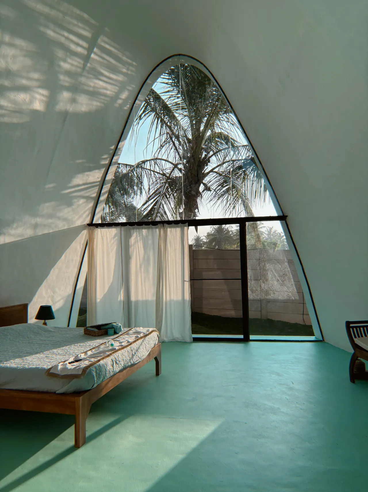 A sunlit villa bedroom inside the shell, with a floor-to-ceiling arched window